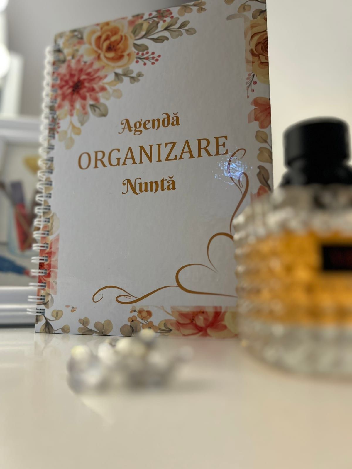 Agenda cu coperta florală, lângă o sticlă de parfum